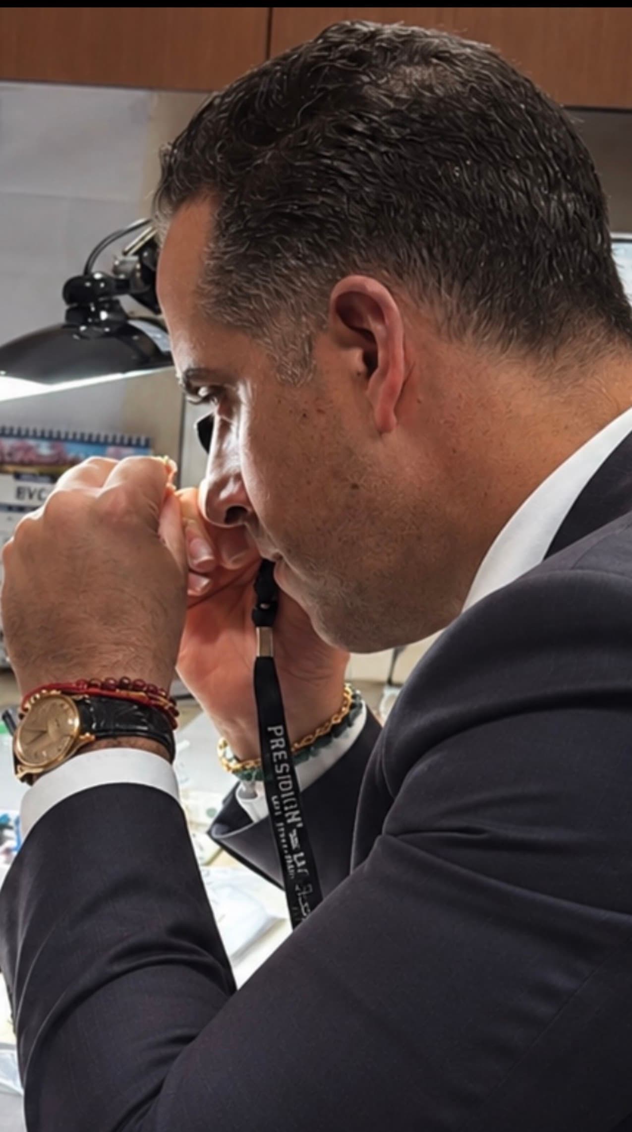 Hombre de perfil con traje examinando minuciosamente un objeto pequeño con una lupa profesional.